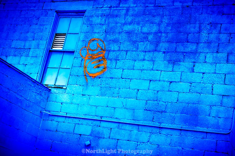 Blue walls, orange graffiti, blue window panes and frames in downtown Ludington, Michigan, USA.